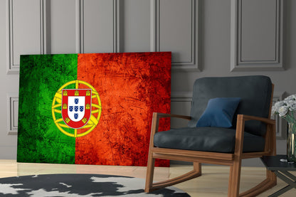 Portuguese flag glass wall art displaying green and red vertical sections with yellow coat of arms, positioned in modern living room next to wooden chair.
