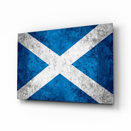 Angled three-quarter view of a rectangular glass panel displaying a distressed blue and white Scottish saltire cross with scratched metal texture throughout.