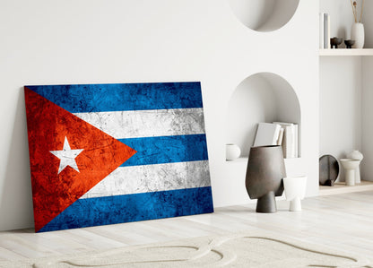 Cuban flag glass wall art leaning against white wall in minimalist interior with decorative objects and shelving.