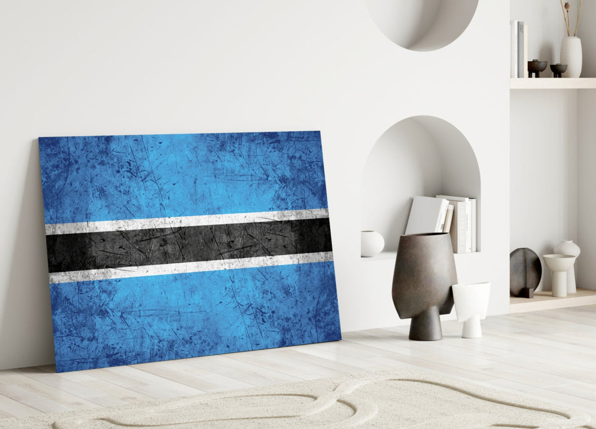 Botswana flag glass wall art leaning against white wall in minimalist room with decorative objects.