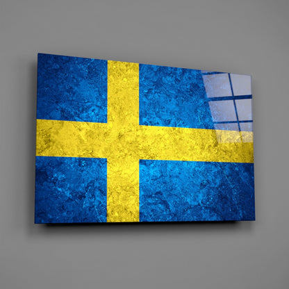Swedish flag glass wall art displayed at an angle against gray wall, showing blue and yellow colors with textured surface.