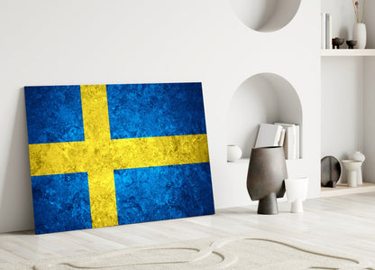 Swedish flag glass wall art leaning against white wall in minimalist interior with decorative objects.