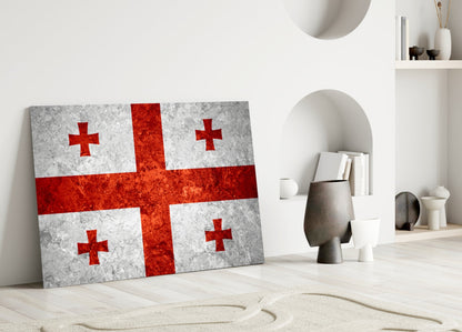 Georgian flag glass wall art leaning against white wall in minimalist interior with decorative objects and shelving.