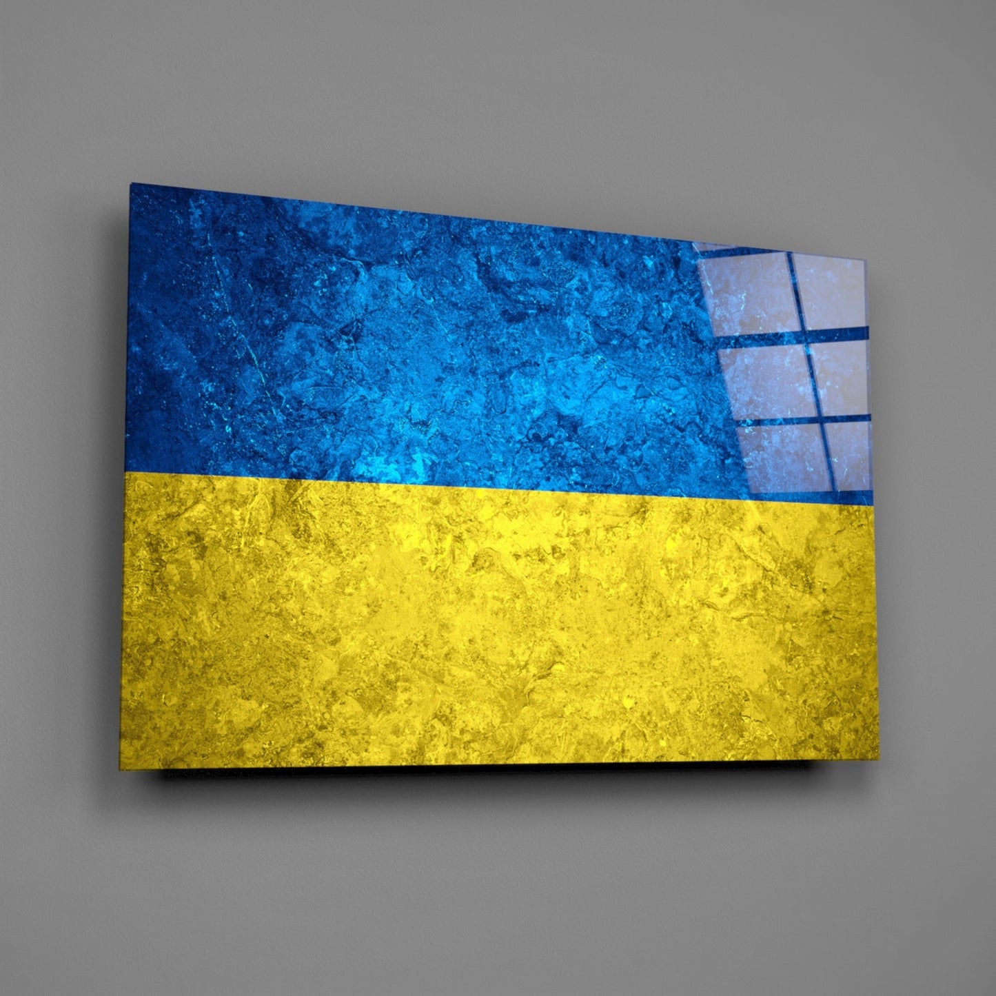Glass wall art displaying Ukraine's flag with blue upper half and yellow lower half, mounted on gray wall at slight angle.