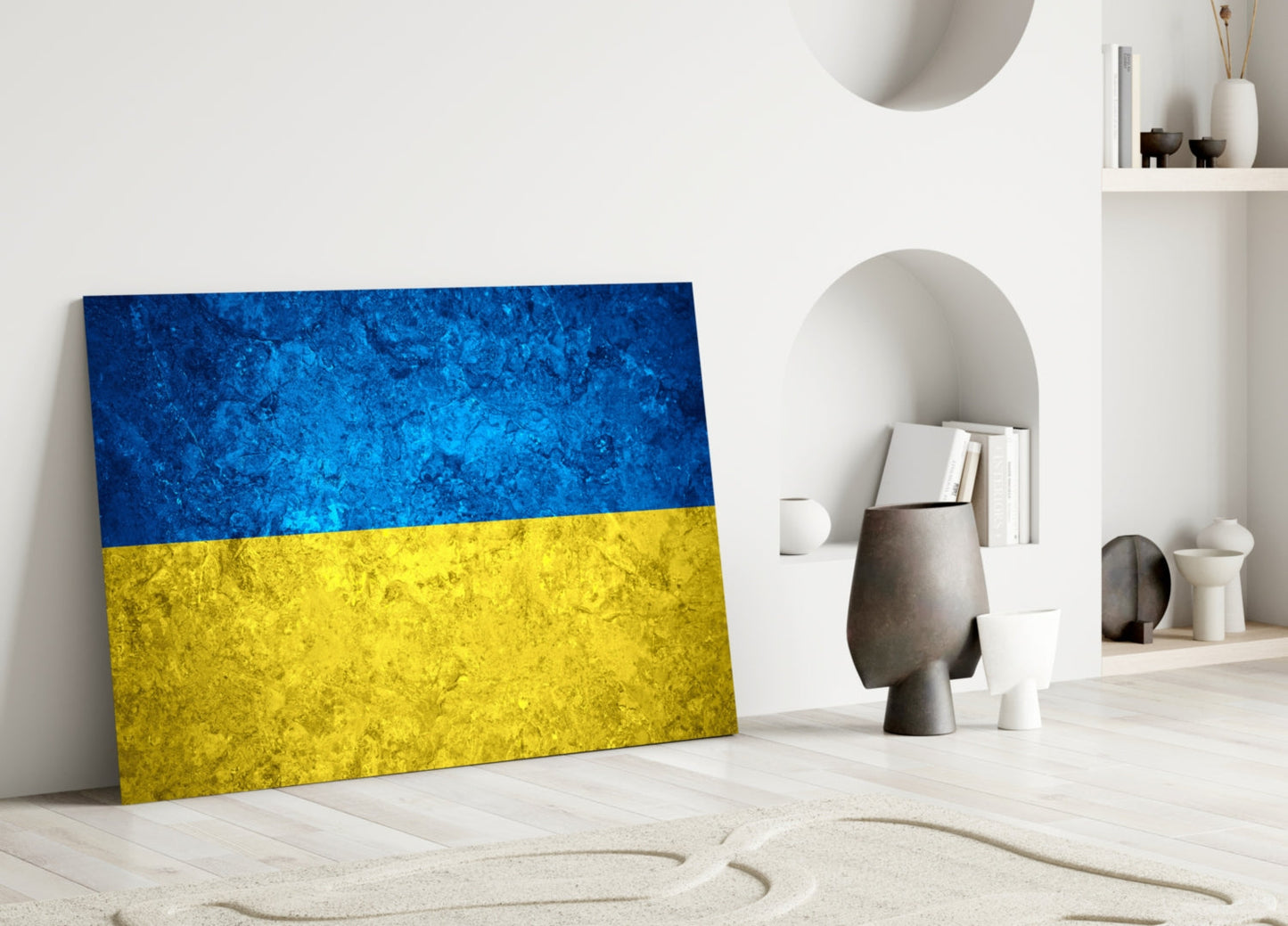 Ukrainian flag glass wall art leaning against white wall in minimalist room setting with decorative objects.