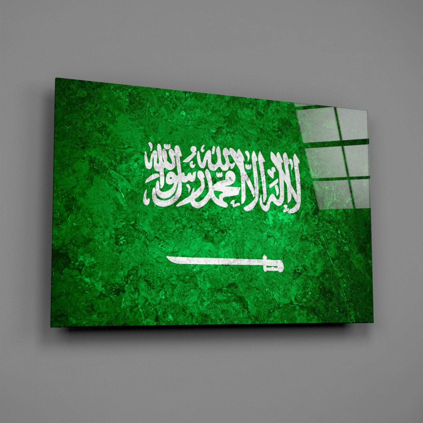 Saudi Arabia flag glass wall art displayed at an angle, showing green background with white Arabic text and sword symbol.