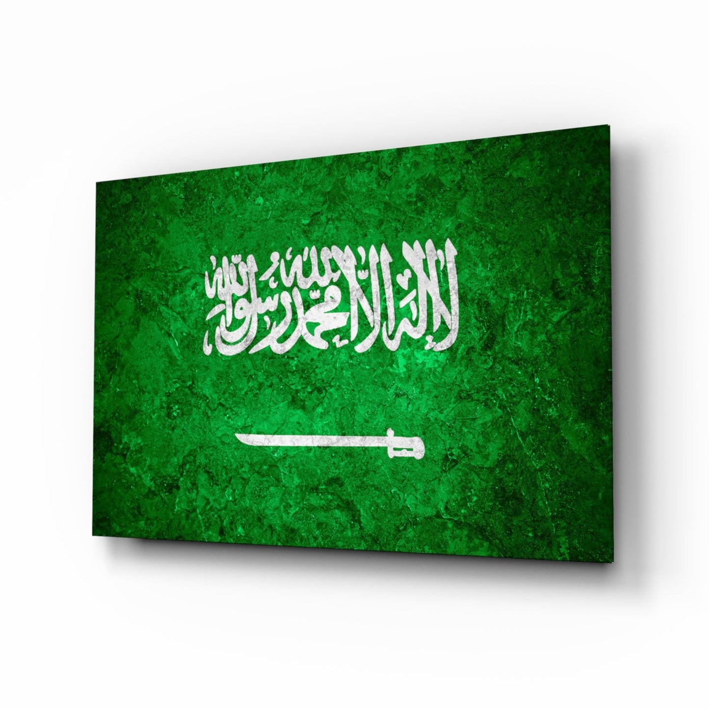 Glass wall art panel displaying Saudi Arabia's flag with green background, white Arabic script, and white sword, photographed at an angle.