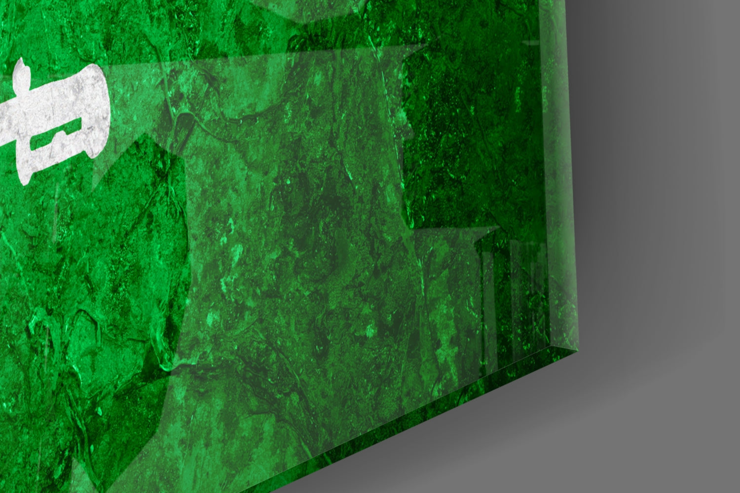 Close-up angled view of green glass wall art featuring white Saudi Arabian flag symbol against textured surface.