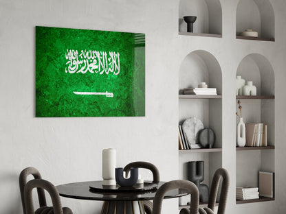 Saudi Arabia flag glass wall art displaying white Arabic text and sword on green background, hung above black dining table in modern interior.