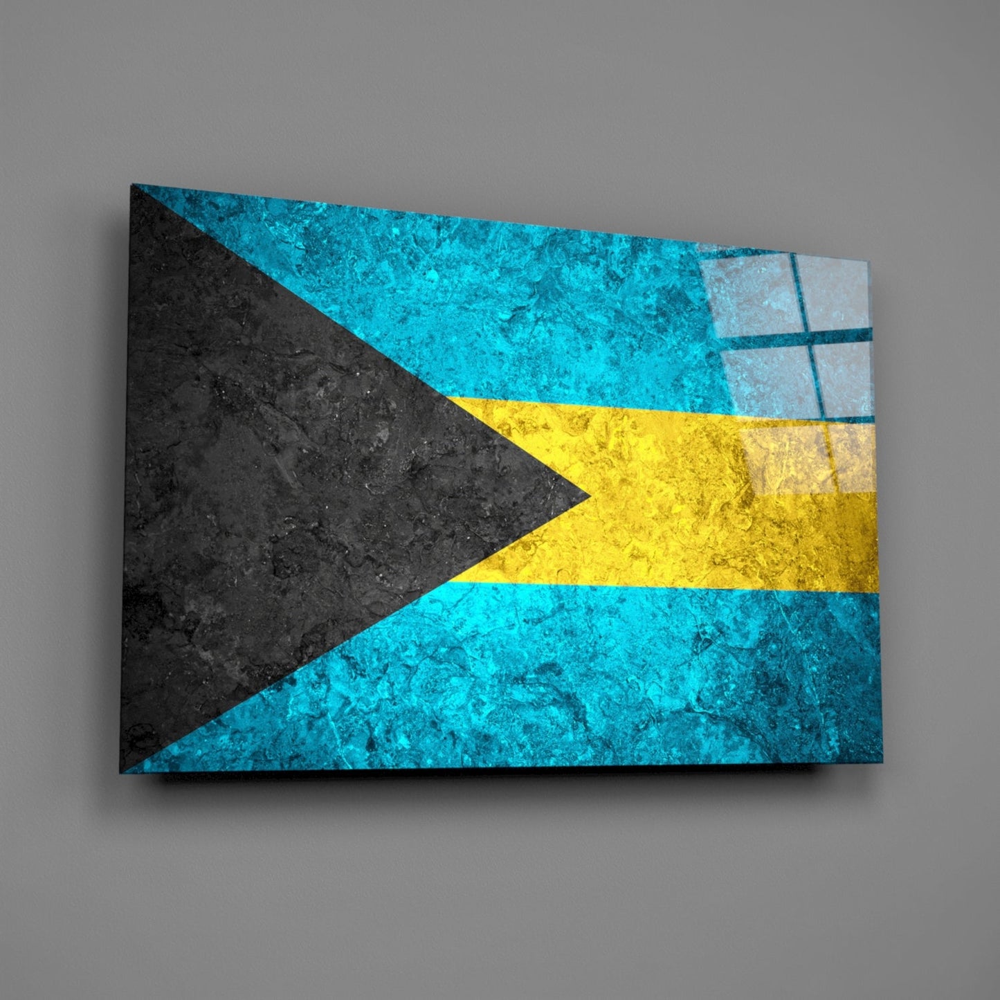 Bahamian flag glass wall art displayed at an angle against a gray wall, showing turquoise, yellow, and black colored stripes with a dark triangular chevron.