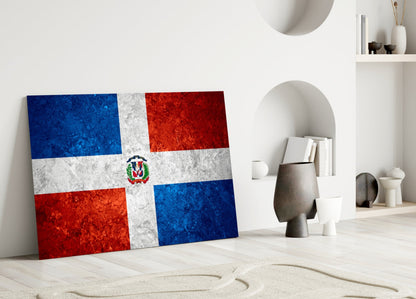 Dominican Republic flag glass wall art leaning against white wall in minimalist interior with decorative objects.