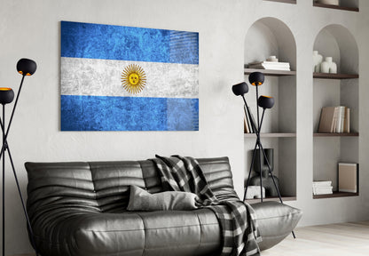 Argentine flag glass wall art displaying blue-white-blue horizontal stripes with golden sun, displayed above black leather sofa in modern living room.