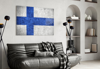 Finnish flag glass wall art with blue cross on white background displayed above black leather sofa in modern living room interior.