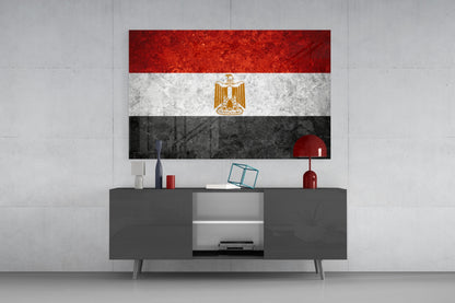 Egyptian flag glass wall art displaying red, white, and black horizontal stripes with gold eagle emblem, mounted above gray media console.
