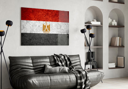Egyptian flag glass wall art displaying red, white, and black horizontal stripes with gold eagle emblem, hung above black leather sofa in modern living room.