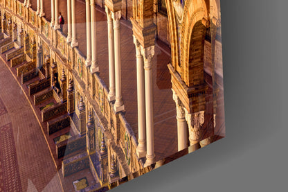 Angled view of glass wall art displaying ornate Spanish colonial architecture with terracotta tiles, white columns, and decorative tilework in warm golden light.