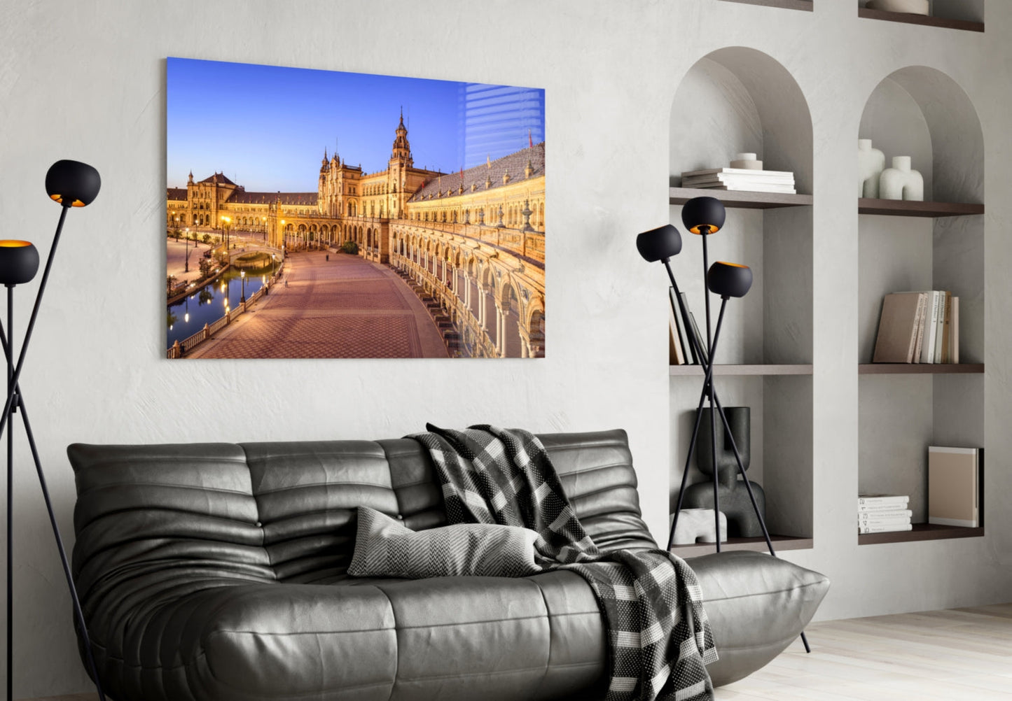 Glass wall art displaying illuminated golden architecture and plaza reflected in water, mounted above black leather sofa in modern living room.