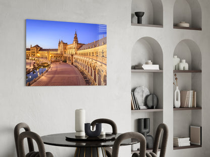 Glass wall art displaying illuminated golden architecture of Plaza de España in Seville, mounted above dining table in modern interior.