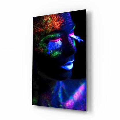 Angled profile view of glass wall art displaying a face with neon makeup in vibrant blue, green, magenta, and orange colors against black background.