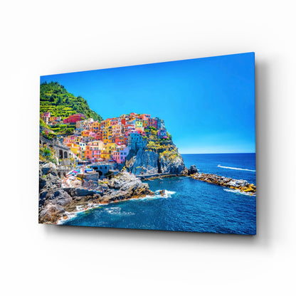 Colorful cliffside village with stacked pastel buildings overlooking blue Mediterranean Sea on glass wall art panel.
