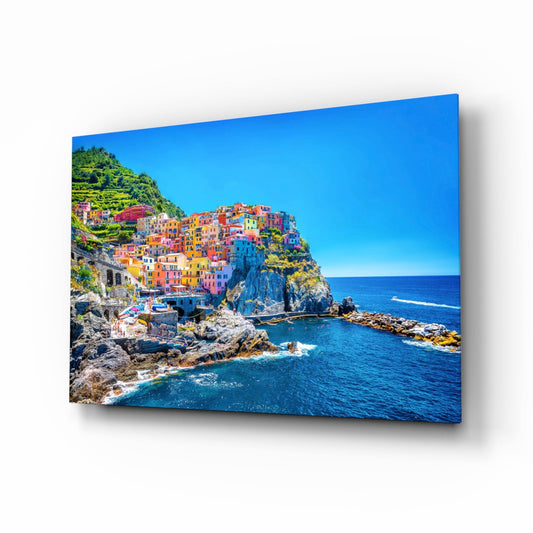 Colorful cliffside village with stacked pastel buildings overlooking blue Mediterranean Sea on glass wall art panel.