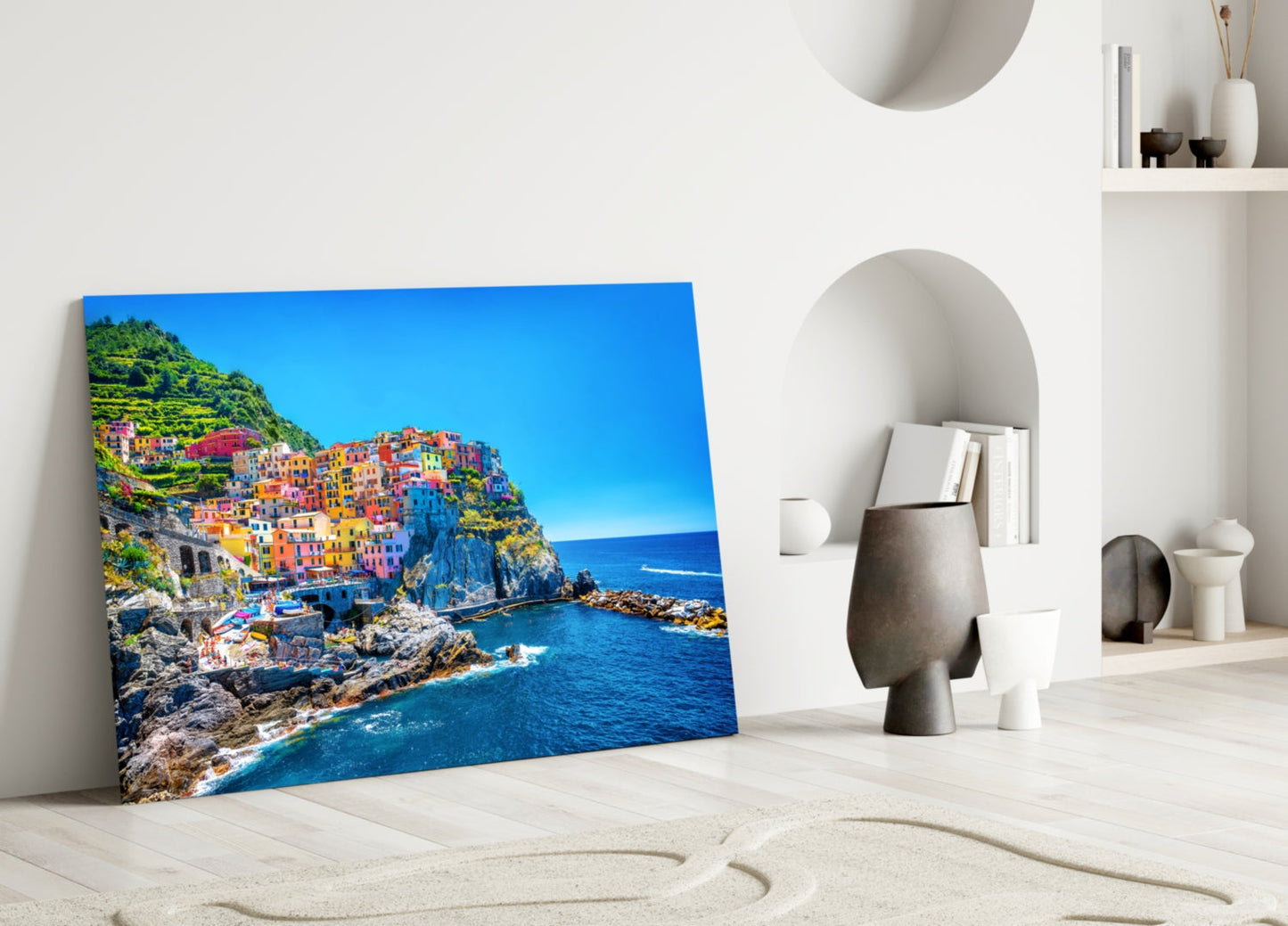 Manarola Glass Wall Art leaning against white wall showing colorful cliffside Italian village with blue sea and sky.