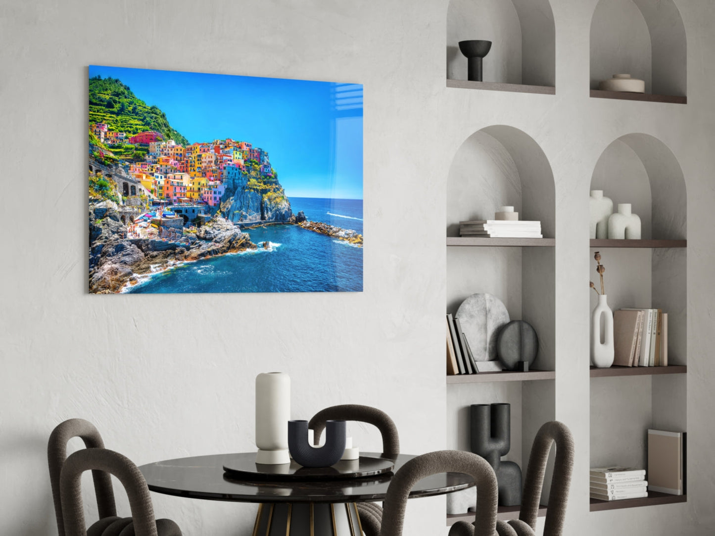 Colorful Italian coastal village with multicolored buildings on rocky cliffside overlooking blue Mediterranean Sea, displayed as glass wall art above round dining table.