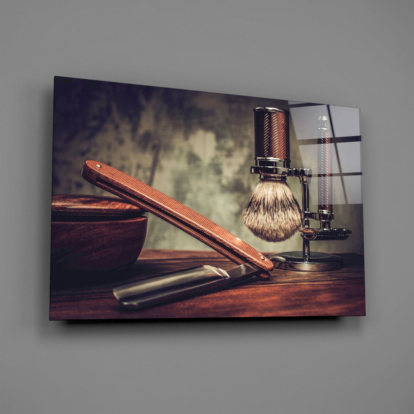 Framed glass wall art displaying vintage shaving tools including a brush, razor, and wooden bowl on a wooden surface.