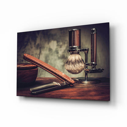 Vintage shaving tools arranged on wooden surface including brush, straight razor, and stand against textured neutral background.