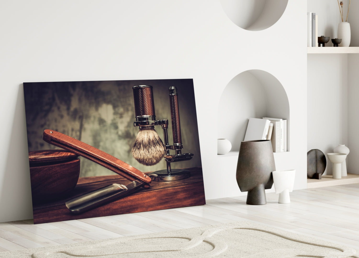 Framed vintage shaving tools artwork leaning against white wall in minimalist interior setting with decorative objects.