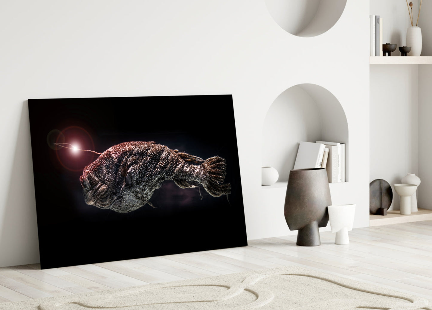 Framed glass artwork leaning against white wall displays bioluminescent deep-sea fish with glowing lure against black background.