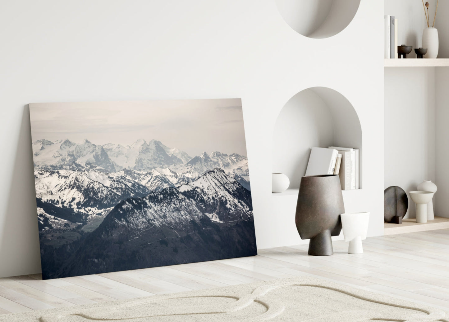 Snowy Mountains Glass Wall Art leaning against white wall in minimalist room with sand, pottery, and shelving.