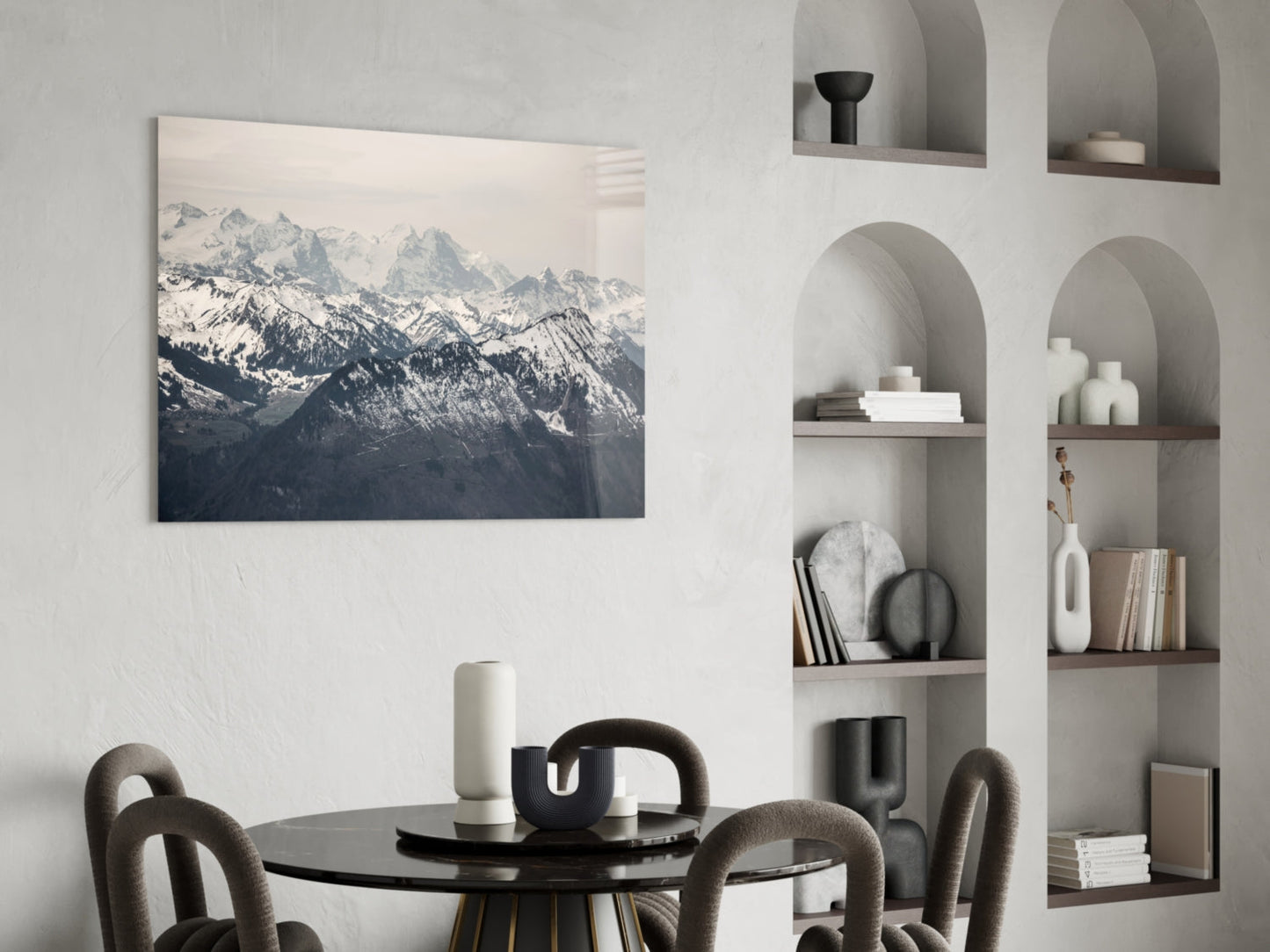 Mountain landscape glass wall art displaying snow-capped peaks displayed above a black dining table with curved chairs.