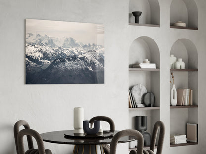 Mountain landscape glass wall art displaying snow-capped peaks displayed above a black dining table with curved chairs.