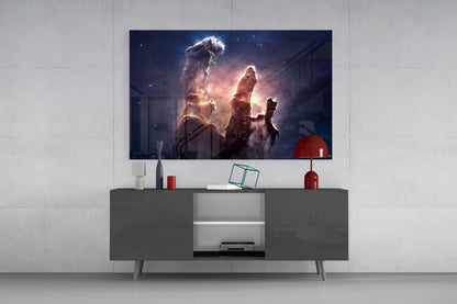 Modern living room setup featuring glowing nebula glass wall art displaying illuminated cosmic dust pillars above a dark gray media console with red decorative accessories.