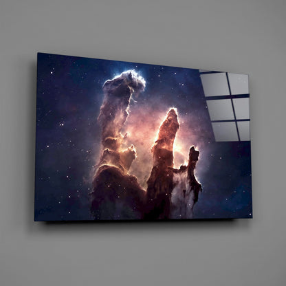 Glass wall art mounted on gray wall displaying illuminated nebula cloud formations in deep blue and amber tones with starfield.