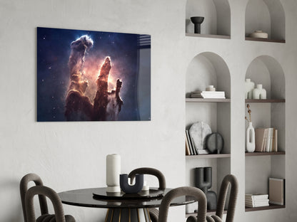 Glass wall art depicting luminous pillars of cosmic dust and gas in deep space, displayed above a round dining table with modern chairs.