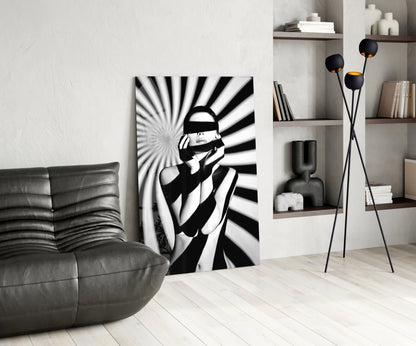 Black and white glass art panel featuring censored figure with radiating lines, displayed in modern living room with gray sofa and shelving.