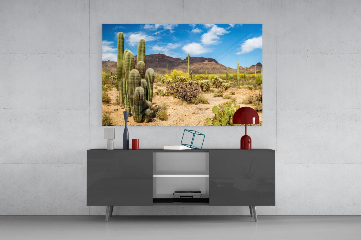 Desert landscape glass wall art depicting tall saguaro cacti displayed above dark modern TV console with decorative accessories.