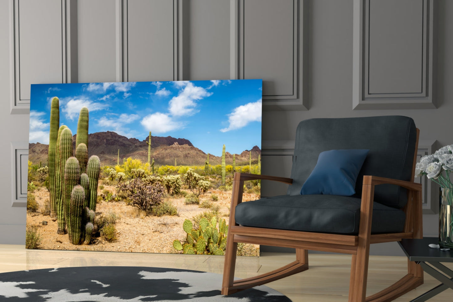 Desert landscape glass wall art depicting saguaro cacti and mountains displayed in a modern living room beside a wooden chair.