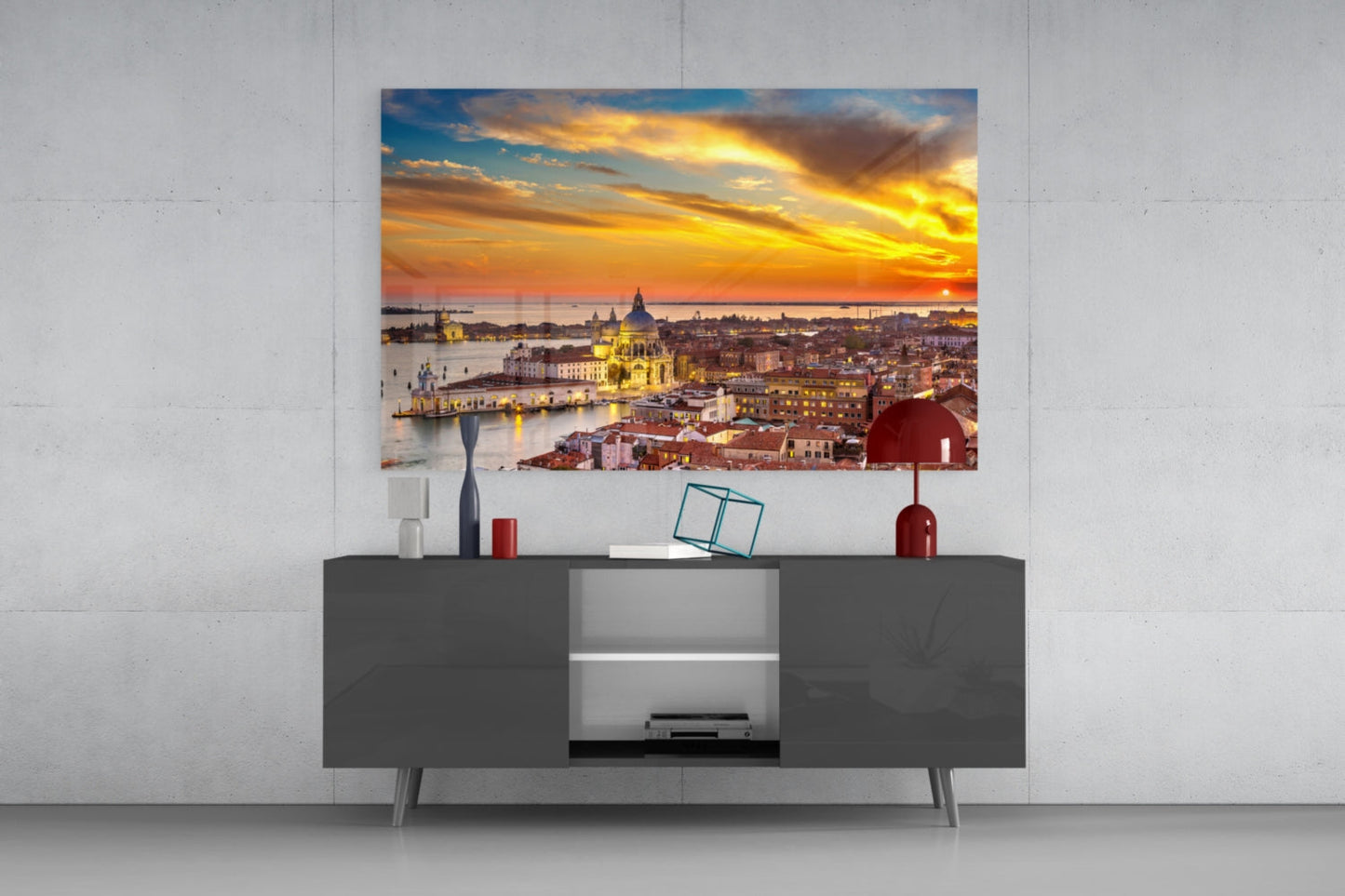 Glass wall art print of Venice sunset displayed above a dark gray media console with decorative accessories.