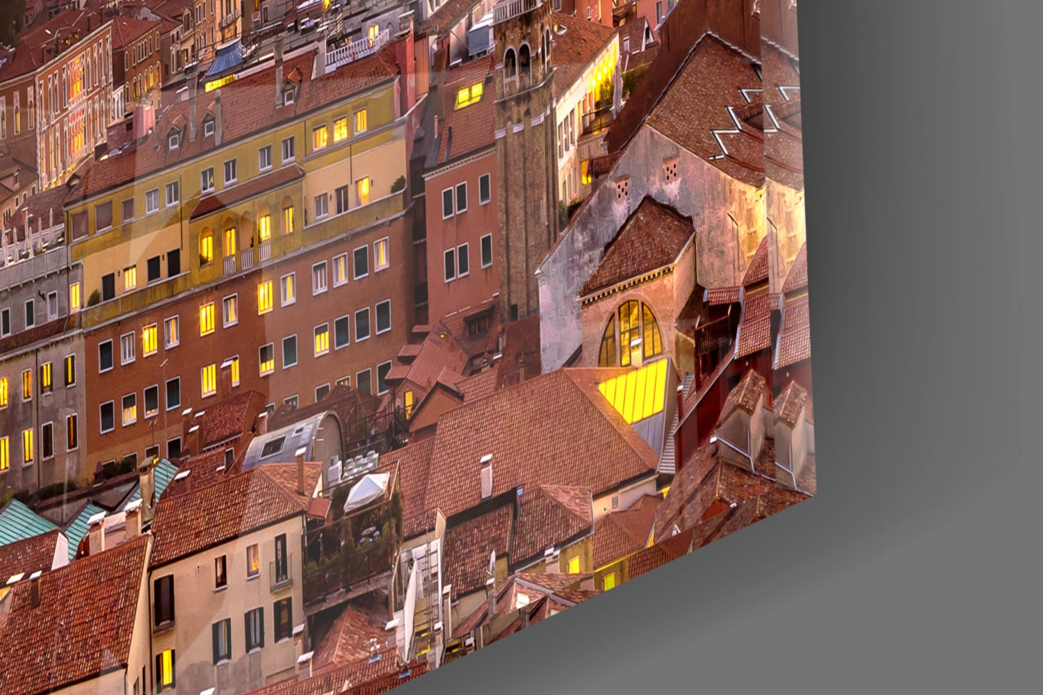 Aerial nighttime view of a European city courtyard with terracotta roofs, brick buildings, and illuminated windows in warm golden tones.