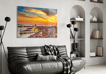 Glass wall art depicting golden sunset over Venice with illuminated basilica, displayed above black leather sofa in modern living room.