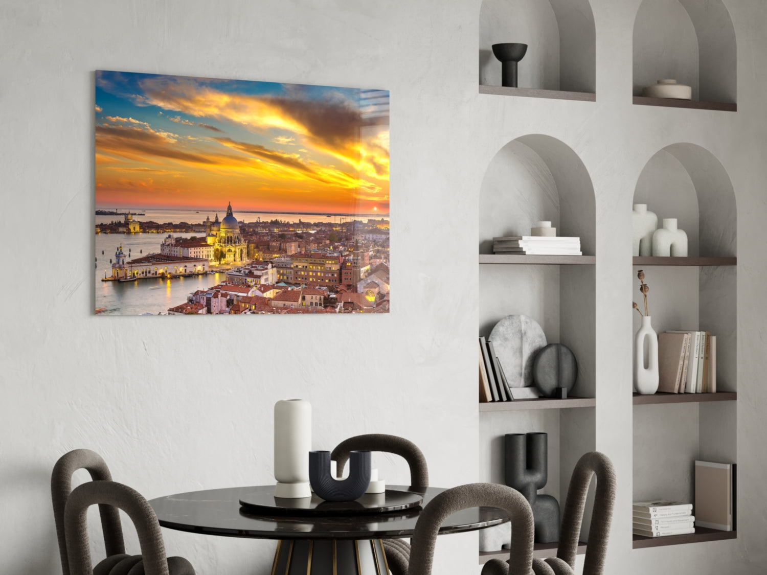 Glass wall art depicting Venice sunset with golden sky, illuminated basilica, and waterfront cityscape hung in modern dining room above black table.