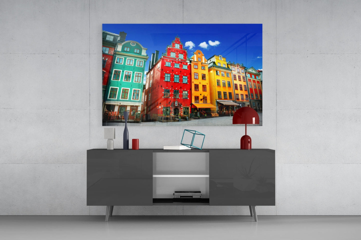 Colorful glass wall art of Stockholm's historic buildings displayed above a dark gray media console in a modern living room setting.