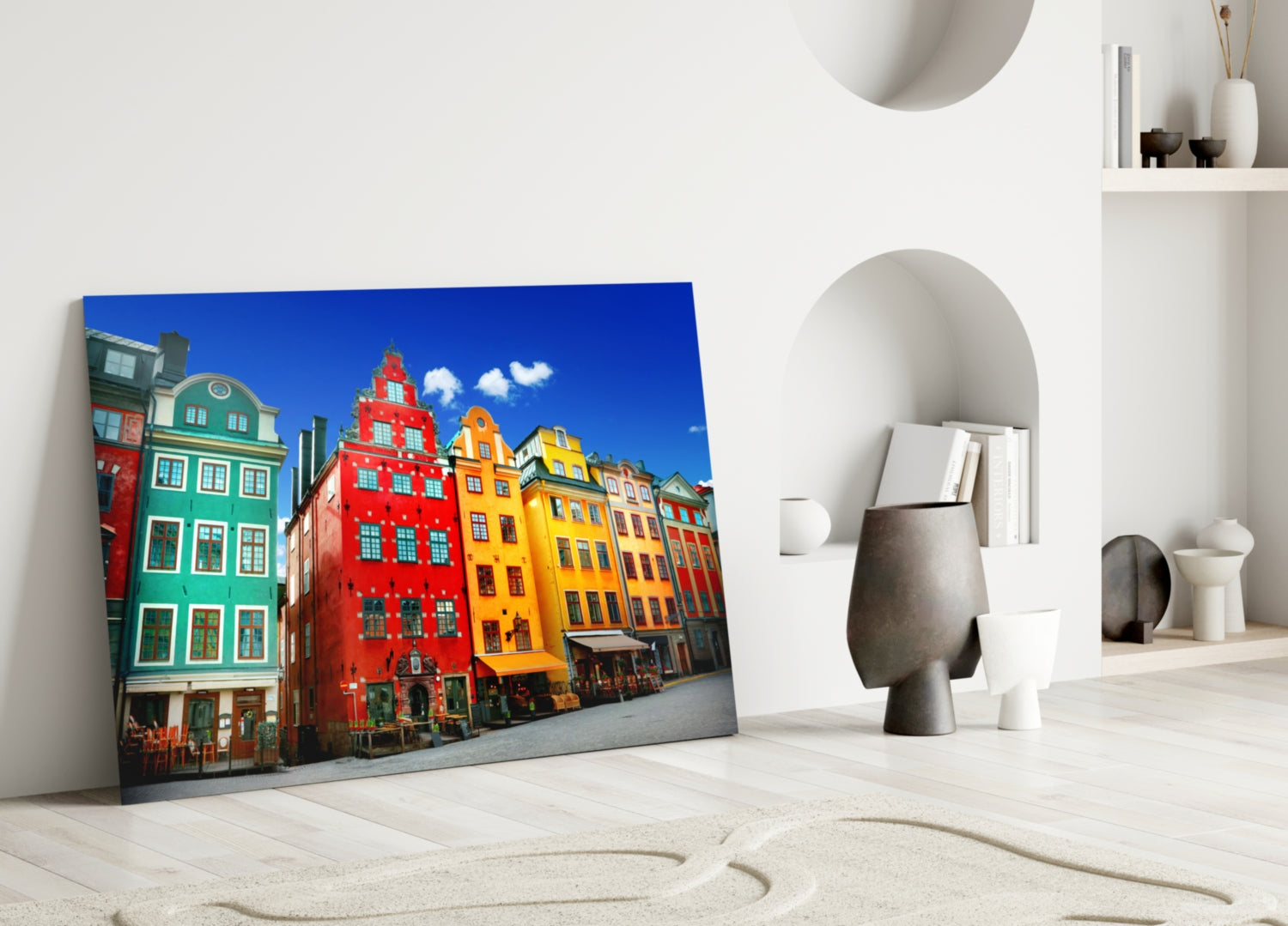 Glass wall art leaning against white wall displaying colorful historic Stockholm buildings in red, yellow, and green under blue sky.