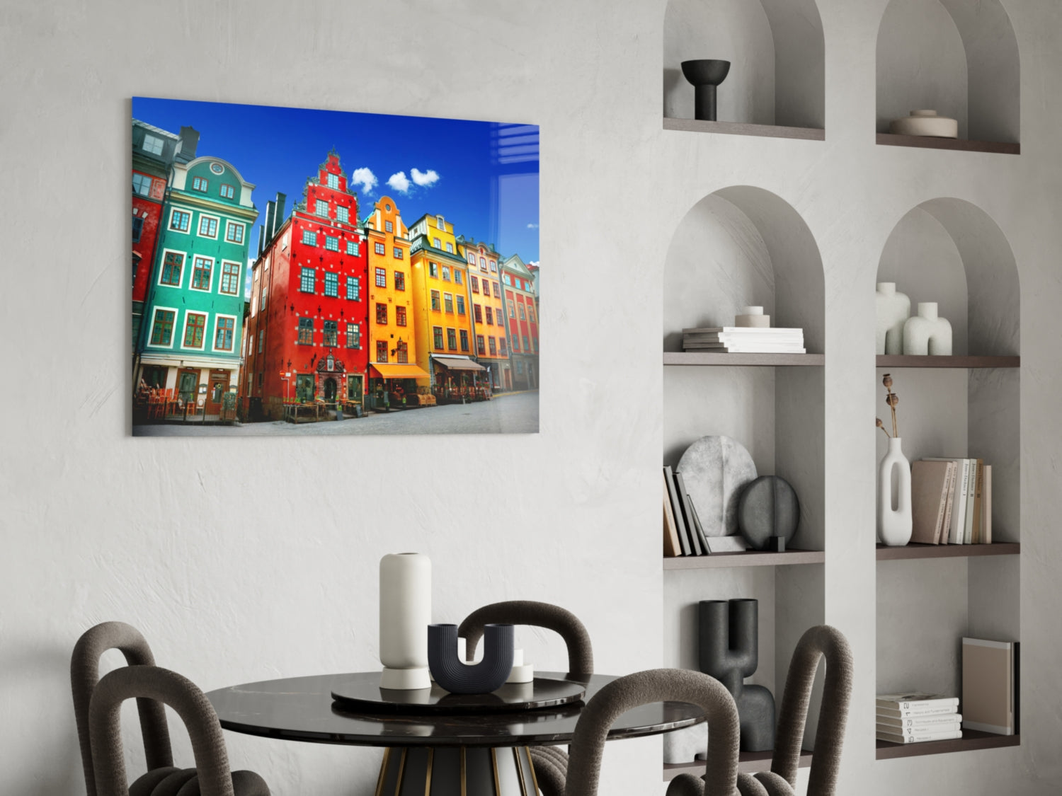 Colorful Stockholm buildings glass wall art displayed above a black round dining table with grey chairs in a modern interior.