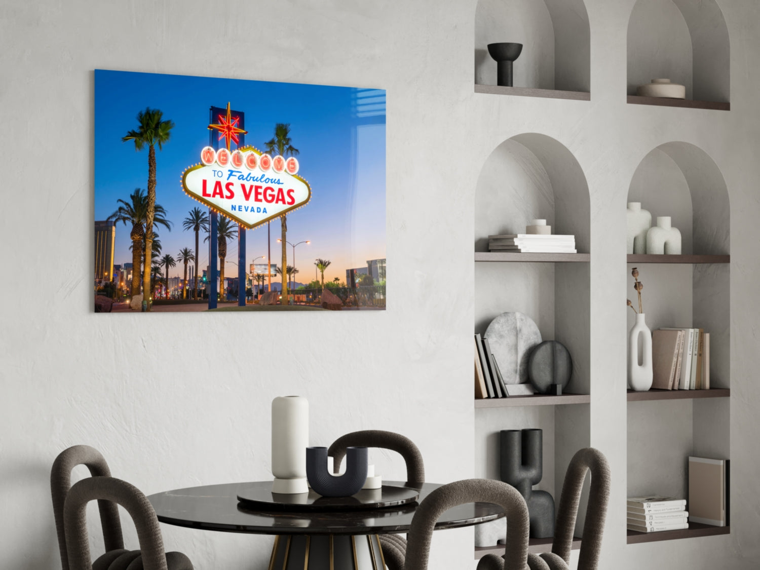 Las Vegas welcome sign glass wall art displayed above a black round dining table in a modern living room with built-in shelving.