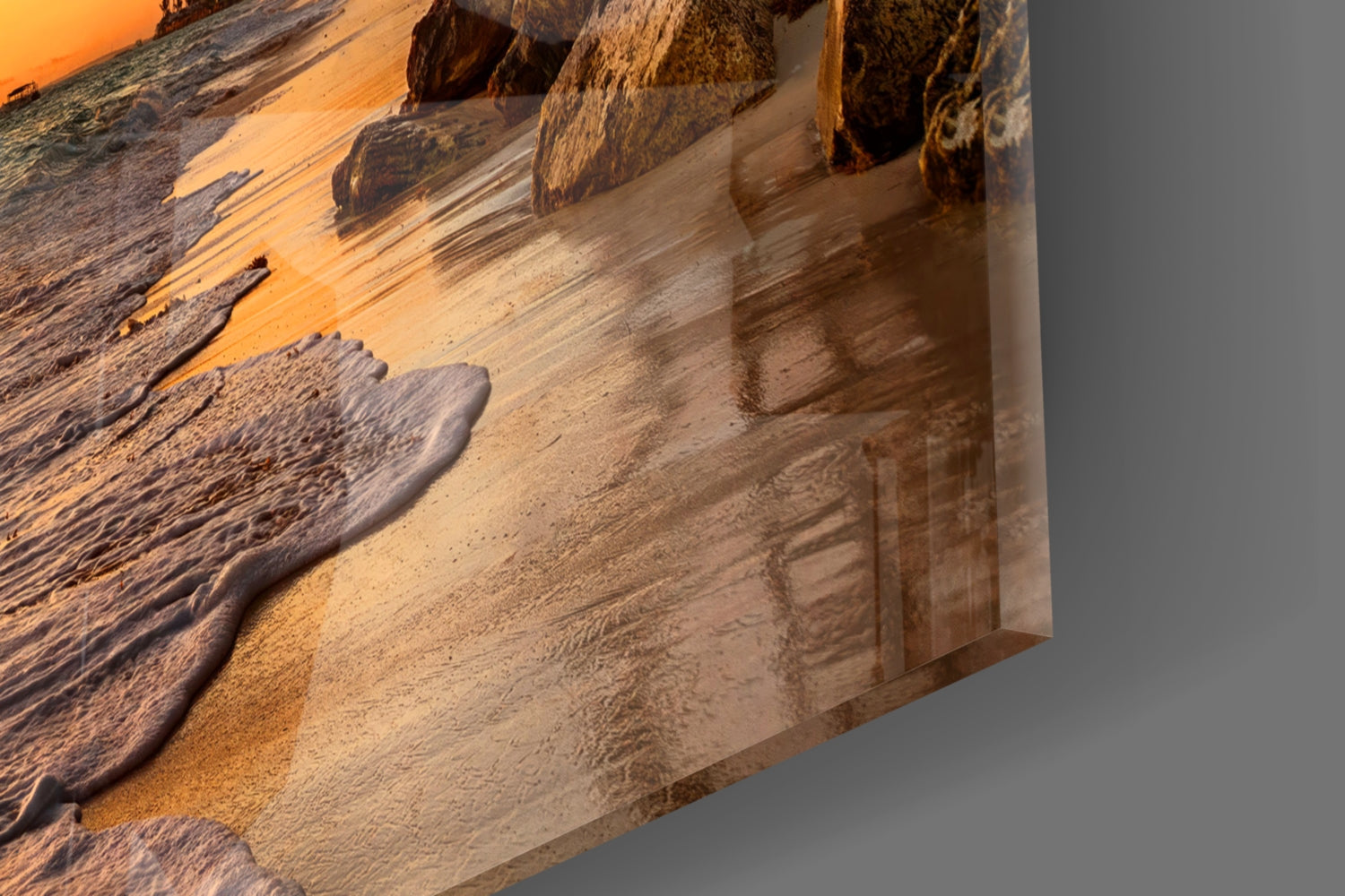 Close-up angled view of glass wall art showing golden sunset beach waves and dark rocks with warm orange lighting.