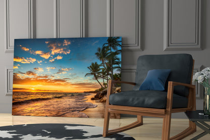 Beach Cruise Glass Wall Art displaying tropical sunset with palm trees and golden ocean waves, displayed in modern living room beside wooden rocking chair.